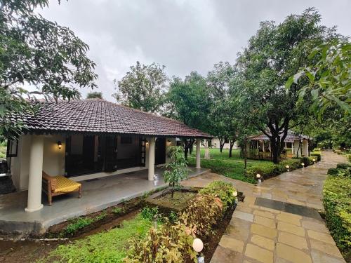 a house with a bench in a yard with trees at SaffronStays Mango Huts by the River, Pali in Jambhulpāda