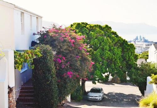 a car parked in a parking lot next to trees with pink flowers at Bougainvillea House - The Heart of Simonstown in Simonʼs Town