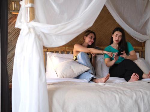 two women sitting on a bed looking at their cell phones at Baan Phuvara Retreat - Romantic Jacuzzi Mountain View Villas in Ao Nang Beach