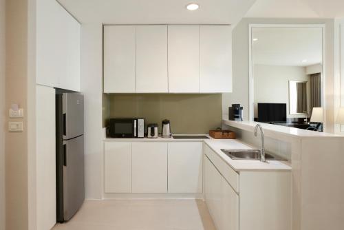 a kitchen with white cabinets and a stainless steel refrigerator at Dusit Suites Hotel Ratchadamri, Bangkok in Bangkok