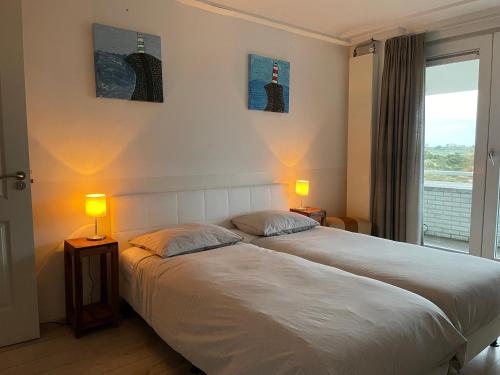 a bedroom with two beds and two lamps and a window at Vitamine Zee in IJmuiden
