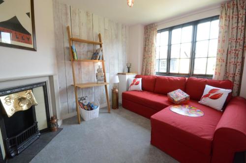 a living room with a red couch and a fireplace at 4 The Dunes, Thorpeness in Thorpeness