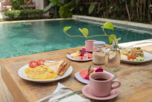 een tafel met borden ontbijtproducten naast een zwembad bij Green Papaya House in Ubud