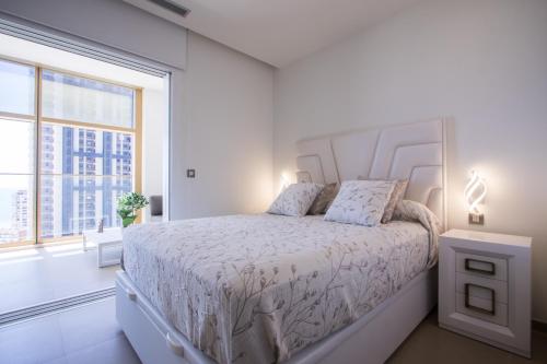 Dormitorio blanco con cama y ventana grande en INTEMPO SKY Apartments 034, en Benidorm