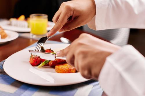 a person eating a plate of food with a fork and knife at Staybridge Suites Dubai Al-Maktoum Airport by IHG in Dubai