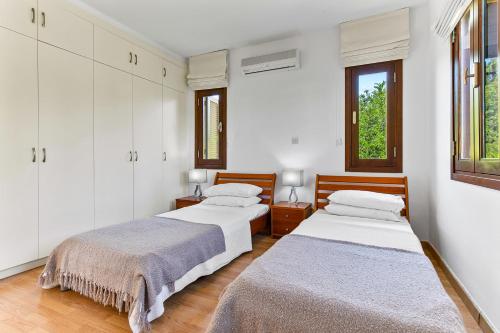 twee bedden in een kamer met witte muren en ramen bij 2 bedroom Apartment Anatoli with communal pool, Aphrodite Hills Resort in Kouklia