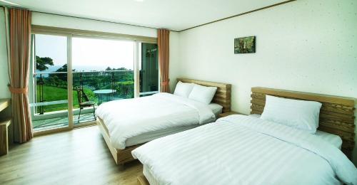 two beds in a room with a large window at Bowhill Resort & Pension in Seogwipo