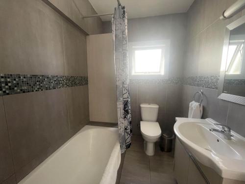 een badkamer met een bad, een toilet en een wastafel bij Christina Apartment in Protaras