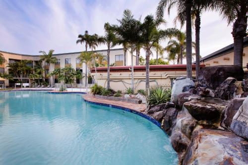 a swimming pool with palm trees in front of a building at Mermaid Waters Hotel by Nightcap Plus in Gold Coast