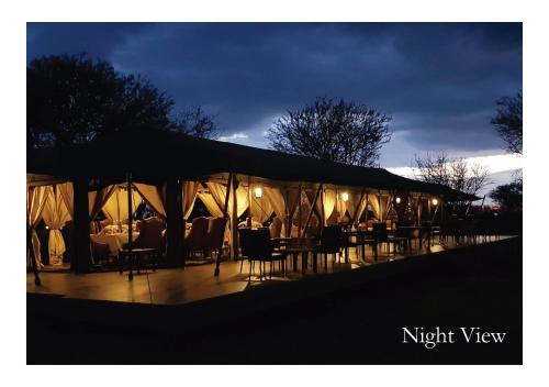 a lit up tent with tables and chairs at night at OLE SERAI LUXURY CAMP - KOGATENDE in Nyanungu