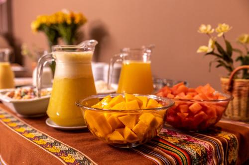Una mesa con jugo de naranja y fruta encima. en Hotel Ferré Boulevard, en Machu Picchu