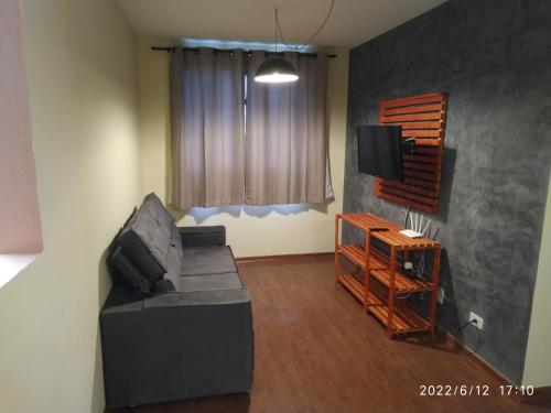 ein Wohnzimmer mit einem schwarzen Sofa und einem TV in der Unterkunft Apto em Curitiba perto de tudo in Curitiba
