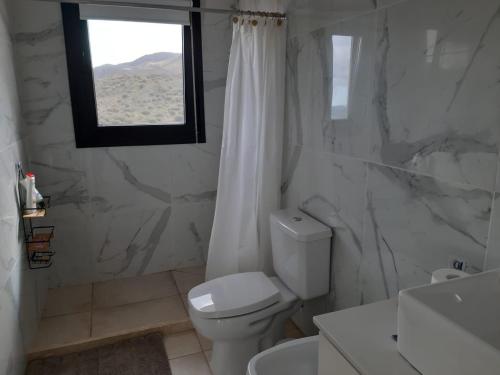 a white bathroom with a toilet and a window at Loft en Rincon de la Cumbre in La Cumbre