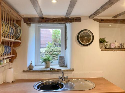 a kitchen sink with a clock and a window at Gem Cottage in Longnor