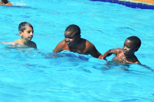 three boys playing in the water in a swimming pool at Forest Park Resort in Buloba