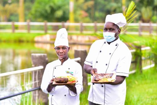 two chefs wearing masks holding plates of food at Forest Park Resort in Buloba