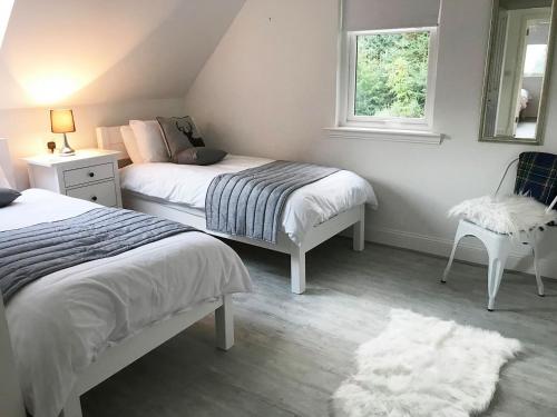 a bedroom with two beds and a chair and a window at Dream Cottage in Strathyre