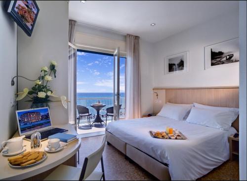 ディアーノ・マリーナにあるHotel La Baiaのベッド、デスク、ノートパソコンが備わるホテルルームです。