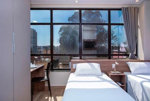 a bedroom with two beds and a desk and a window at GoÁtica Aeroporto Congonhas in Sao Paulo