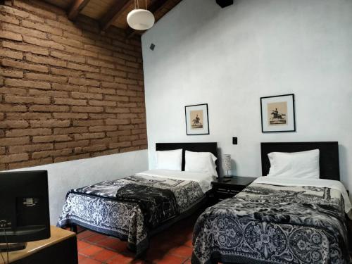 a bedroom with two beds and a tv and a brick wall at Cabañas y habitaciones Los Cedros in Zacatlán