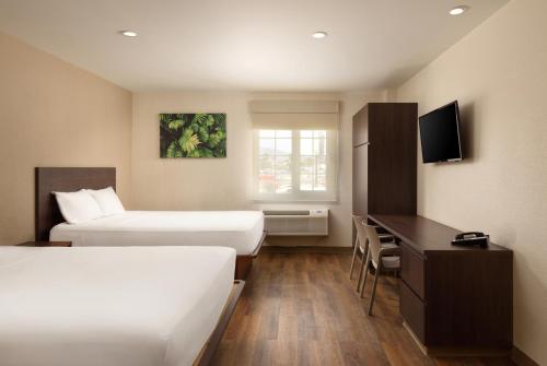 Habitación de hotel con 2 camas, escritorio y TV. en Extended Suites Merida Siglo XXI en Mérida