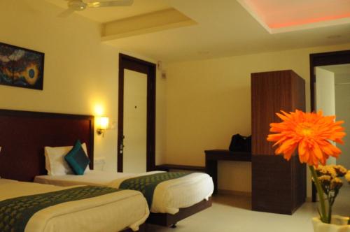 a hotel room with two beds and a vase with an orange flower at Ixora Suites in Bengaluru