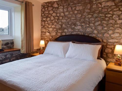 a bedroom with a large bed with a stone wall at Augustus Cottage in Rowlstone