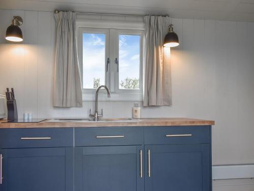 cocina con armarios azules, fregadero y ventana en Gorse - Ukc5327 en Halvergate
