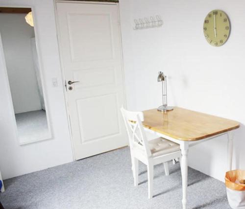 uma mesa e cadeira num quarto com um relógio em Dejligt værelse lyst og hyggeligt em Skovlunde