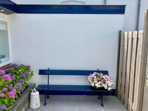 a blue bench sitting next to a white wall with flowers at Have a nice stay! - Beachhouse Stranddistel 100m from the beach in Noordwijk aan Zee
