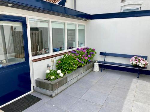 a porch with a bench and flowers next to a building at Have a nice stay! - Beachhouse Stranddistel 100m from the beach in Noordwijk aan Zee