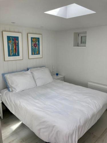 a white bed in a bedroom with two pictures on the wall at Have a nice stay! - Beachhouse Stranddistel 100m from the beach in Noordwijk aan Zee