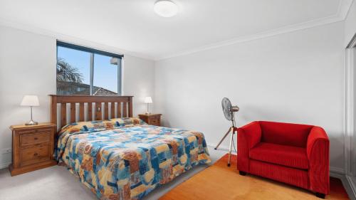 a bedroom with a bed and a red chair at Ocean Palms Unit 2 in The Entrance