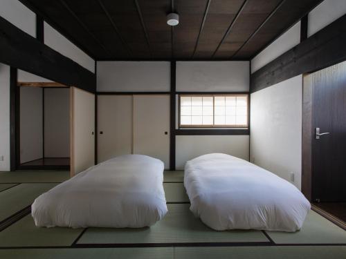 2 weiße Betten in einem Zimmer mit Fenster in der Unterkunft 古民家の宿 Solii in Ishikari
