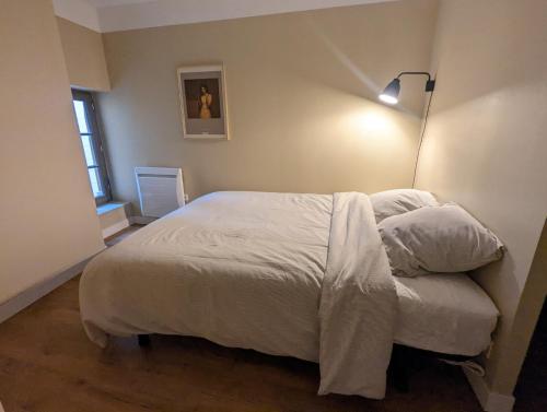 a bedroom with a bed with white sheets and a lamp at Le 5 bis, une maison de ville dans le centre historique in Saint-Galmier