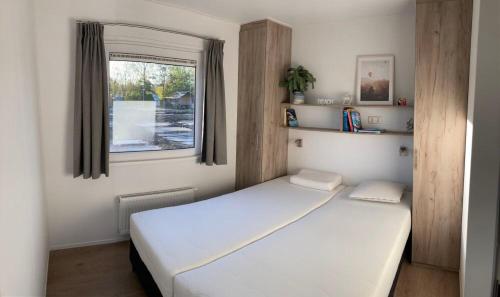 1 dormitorio con cama blanca y ventana en Vakantiepark duinzicht, en Koudekerke