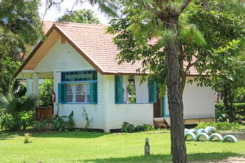 Pai Flora Resort في باي: بيت ابيض صغير بنوافذ زرقاء وشجرة