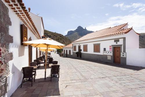 a patio with an umbrella and chairs and buildings at Casa Isabela with Roque Nublo view in Tejeda