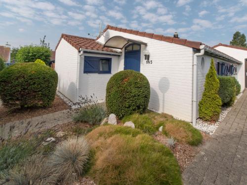 a white house with a blue door and some bushes at Holiday Home Zeewind 145 by Interhome in Bredene