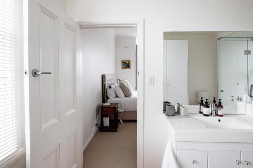 a white bathroom with a sink and a bed at Bridport Beach House in Bridport