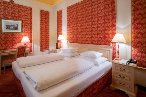 a bedroom with a large white bed with red wallpaper at Hotel König von Ungarn in Vienna