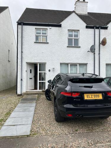 a black car parked in front of a white house at Ballycastle, Strand Cottages Modern Home in Ballycastle