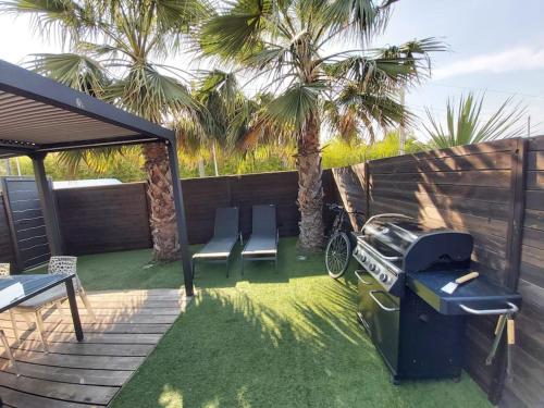 um quintal com duas cadeiras e um grelhador e palmeiras em STUDIO LUXE 600M PLAGE AVEC SPA POUR 4 PERS em Cap d'Agde