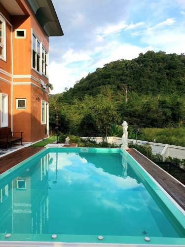 a swimming pool next to a building with a mountain in the background at Chateau de Luxi Khao Yai - ชาโตว์ เดอ ลูซี่ เขาใหญ่ in Mu Si
