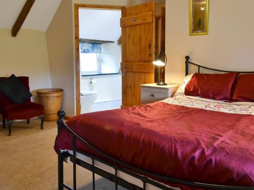 sypialnia z czerwonym łóżkiem i krzesłem w obiekcie Knotty Corner Cottage w mieście Abbotsham