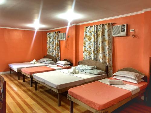 three beds in a room with orange walls at Cardo Homestay Siargao in General Luna