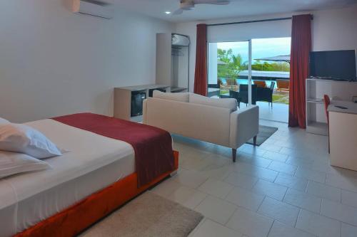 um quarto com uma cama, um sofá e uma televisão em Nosy Be Sun Hôtel em Nosy-Be