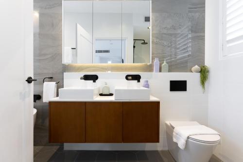 a bathroom with a sink and a toilet and a mirror at Barangaroo Park Apartments by Urban Rest in Sydney