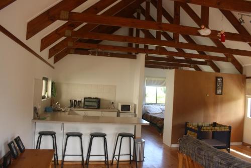 a living room with a kitchen and bar with bar stools at Fijnbosch Cottage and Camping in Stormsrivier