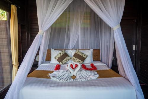 a bed with white curtains and red flowers on it at KiBata Lembongan Boutique Hotel in Nusa Lembongan